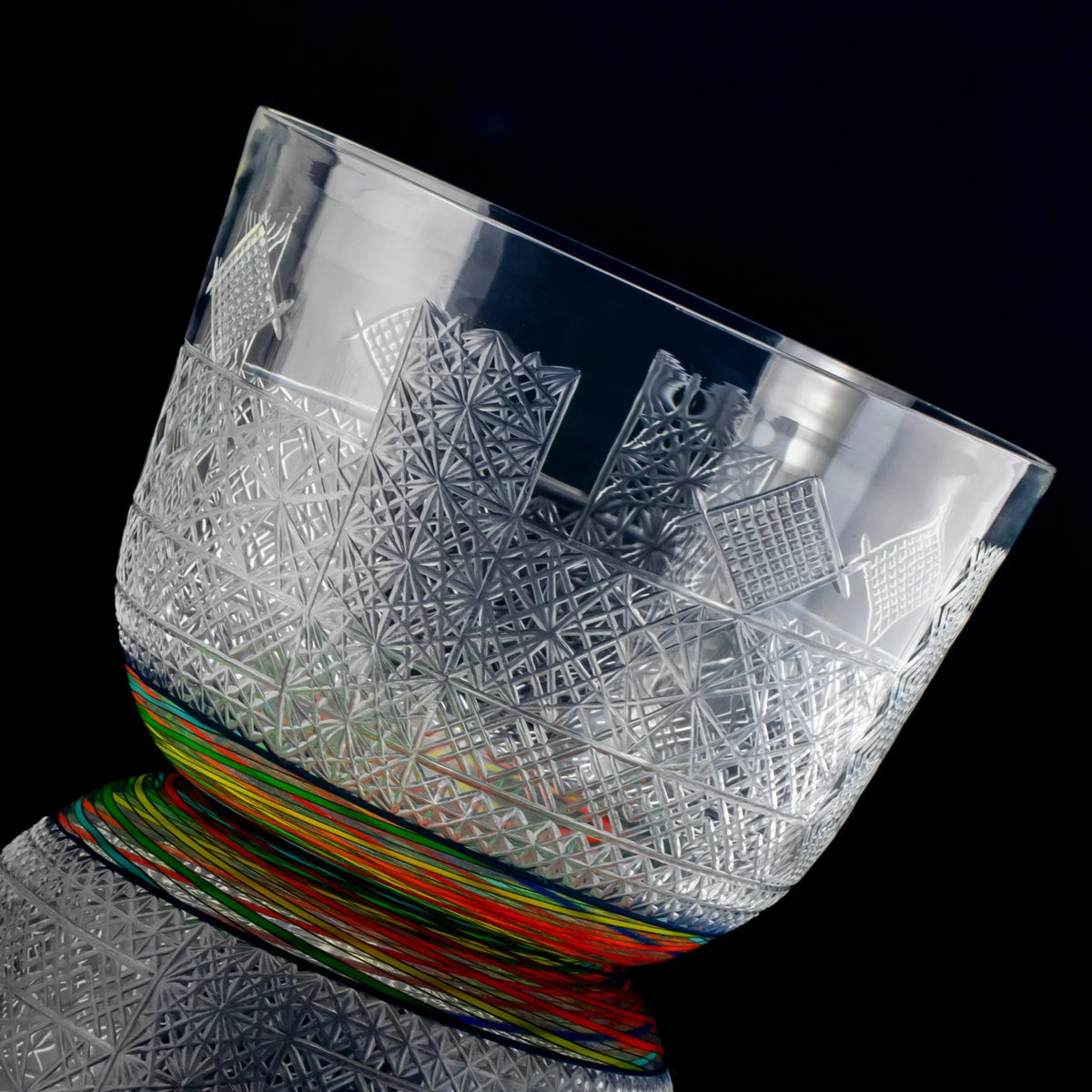 Intricately etched glass bowl with geometric patterns and colorful base on black background