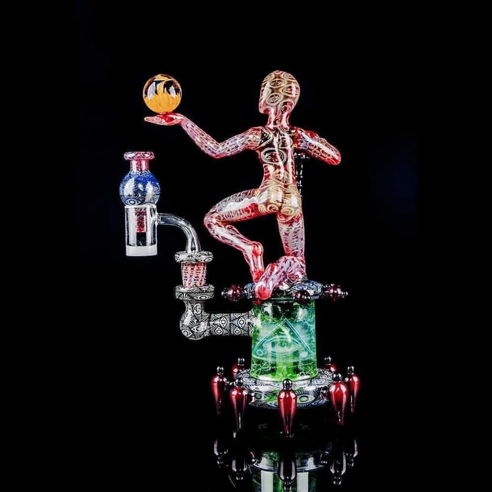 Intricate heady glass dab rig with colorful humanoid figure and artistic details on black background.