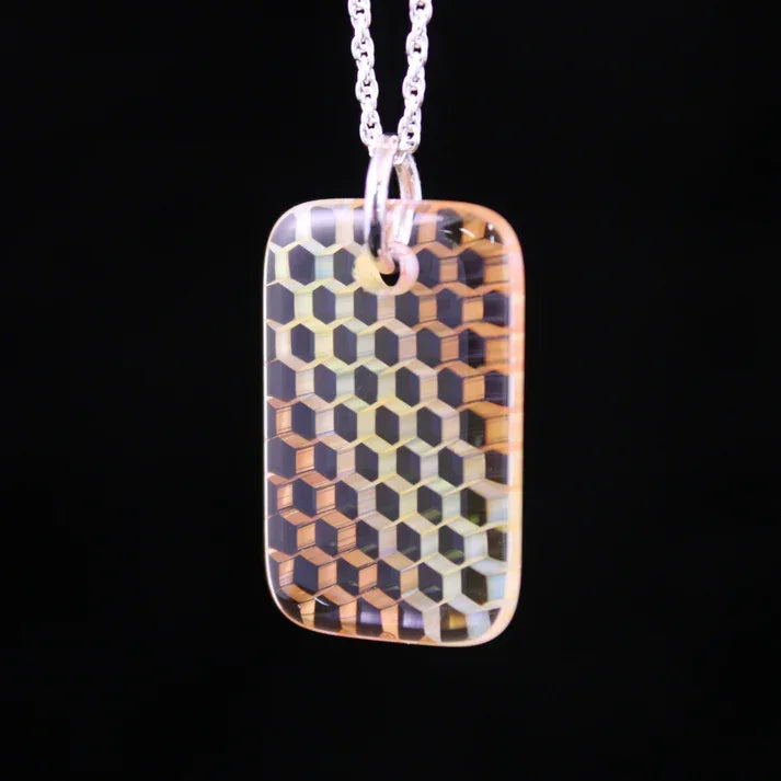 Geometric patterned glass pendant with hexagonal design on a silver chain, black background