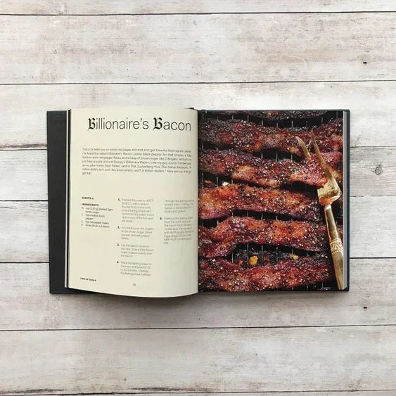 Open cookbook displaying Billionaire’s Bacon recipe with caramelized bacon strips and fork.