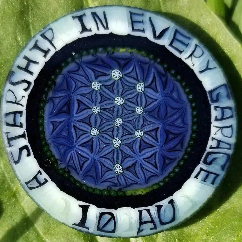 Handcrafted glass medallion with intricate blue geometric pattern and inscription, on green background