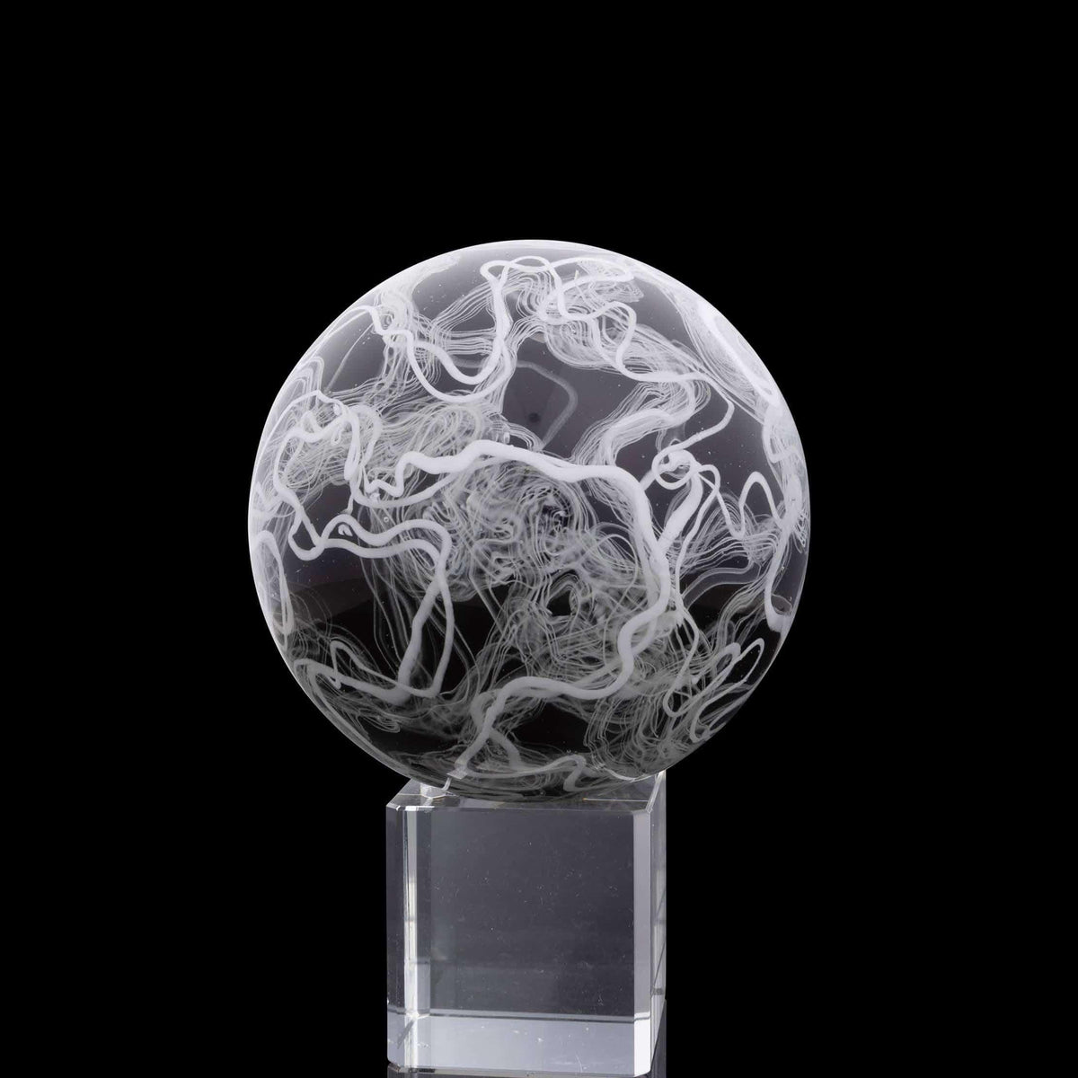 Hand-blown glass marble with white swirling patterns on clear stand, black background