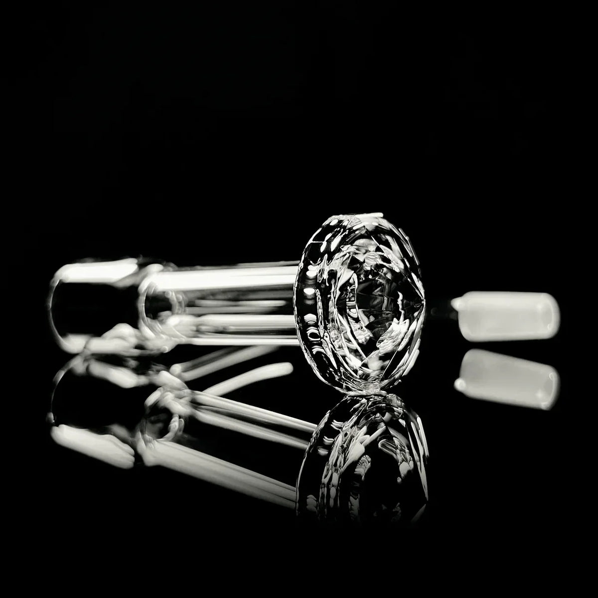 Clear glass water pipe attachment with intricate design on black reflective surface