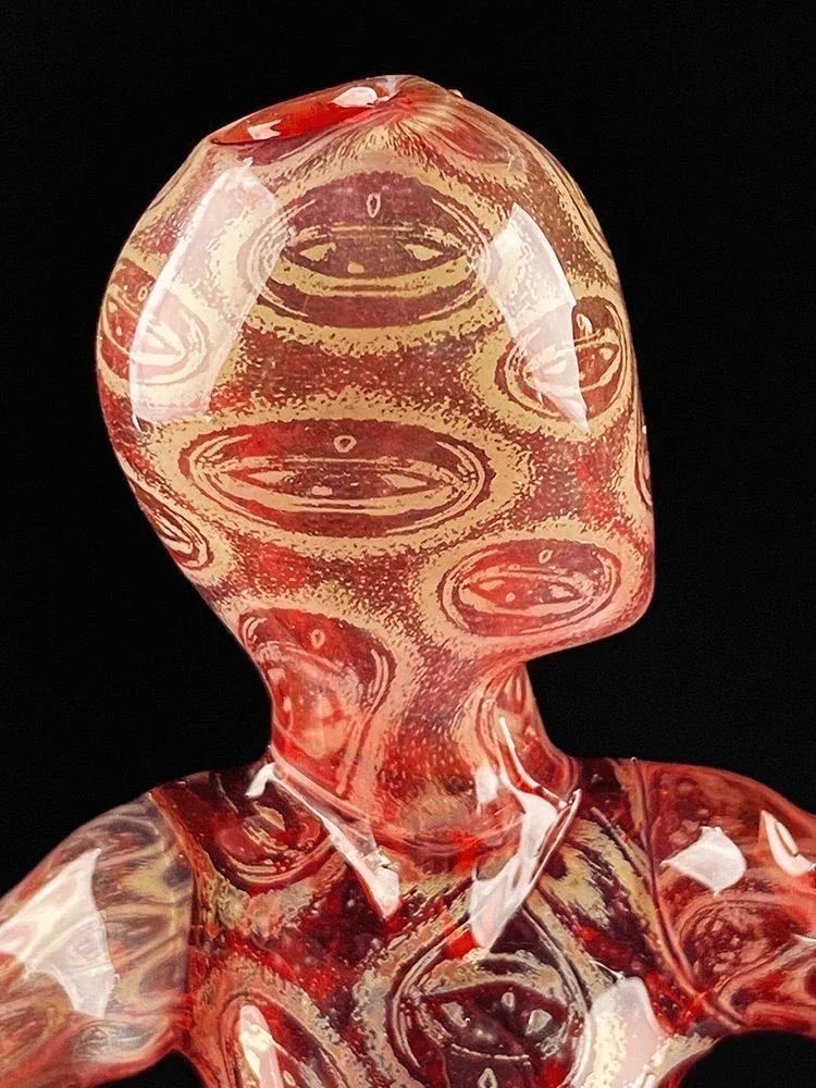 Close-up of a red patterned glass figurine with abstract eye designs, black background