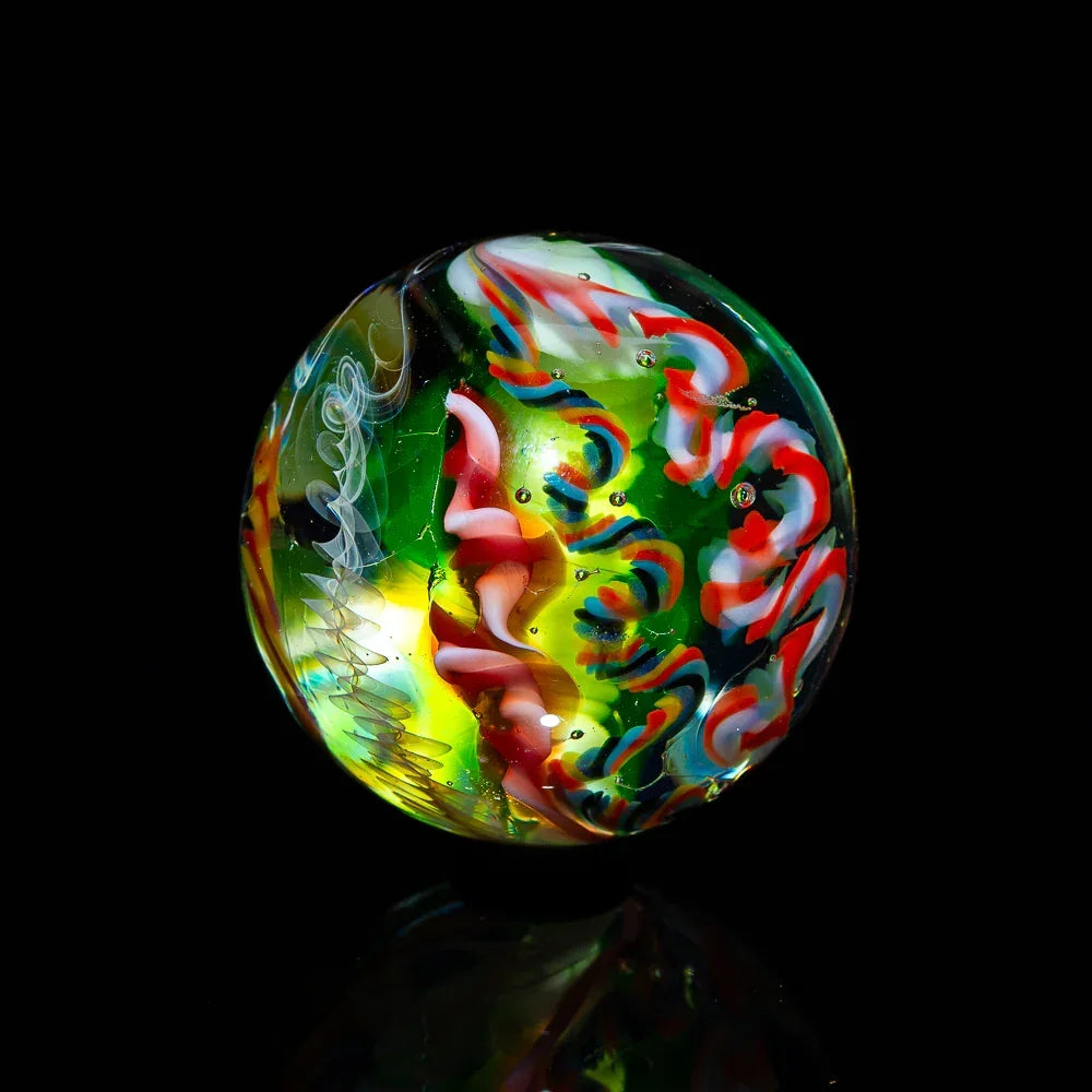 Hand-blown glass marble with vibrant red, green, and yellow patterns on black background