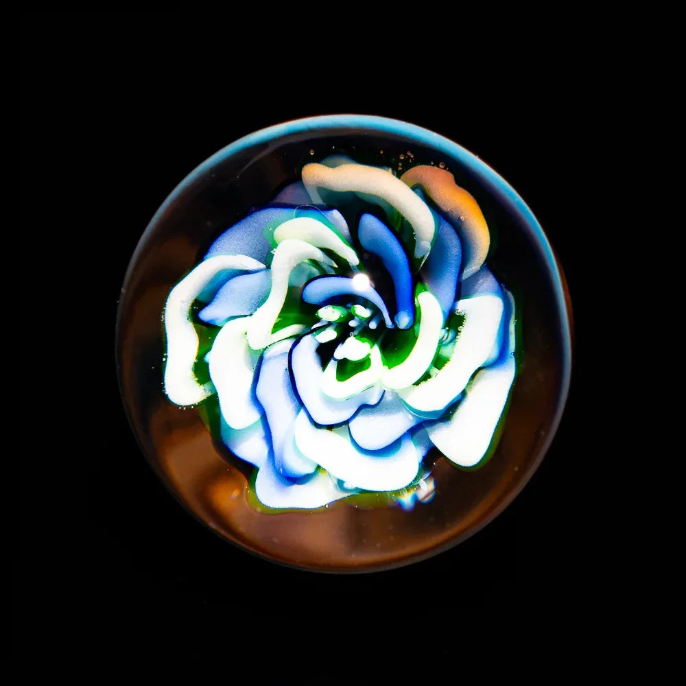 Handcrafted glass marble with intricate blue and white floral design on black background