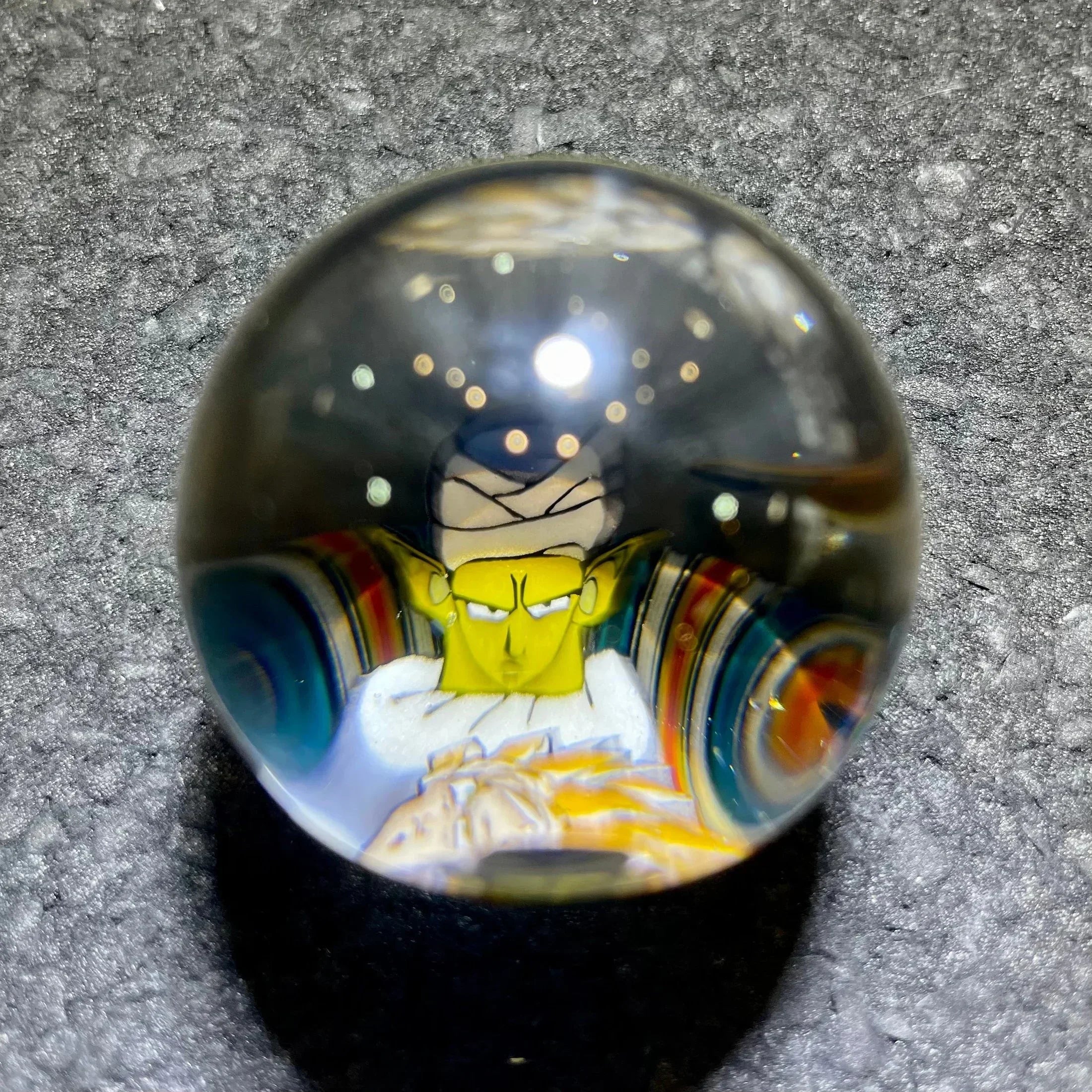 Handmade glass marble featuring colorful character art on a textured gray surface