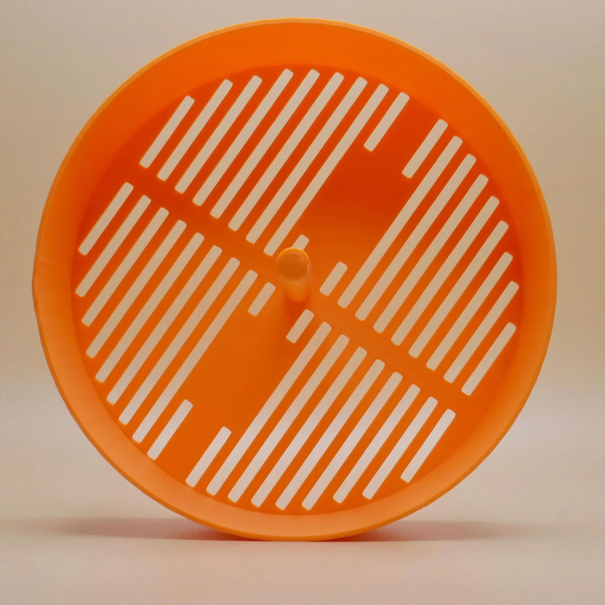 Orange plastic grinder screen insert for herb or spice accessories, ventilation slits visible