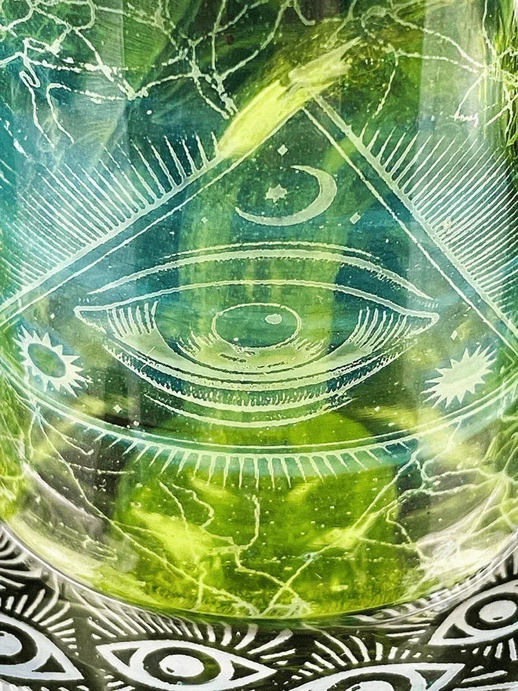 Close-up of glass art with all-seeing eye, moon, and sun etching, green background