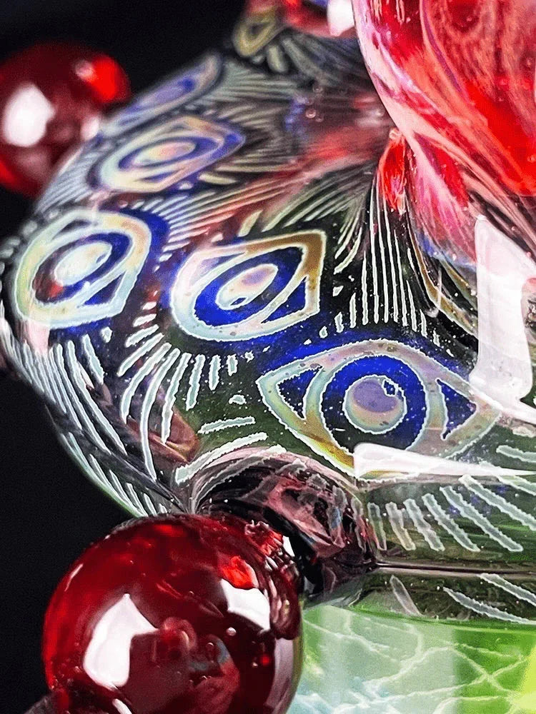 Close-up of intricate glass pipe with peacock-feather patterns and red decorative marbles