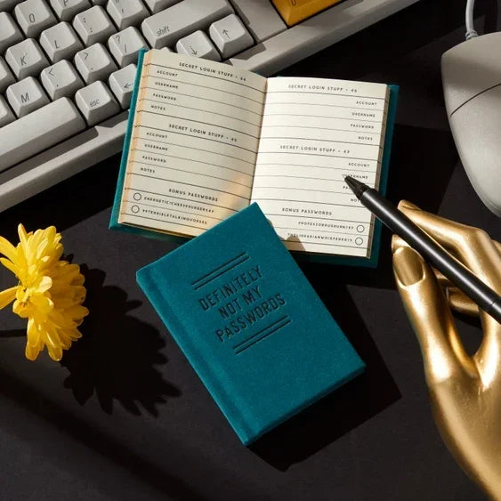 Password organizer notebook on desk with keyboard, pen, and decorative gold hand