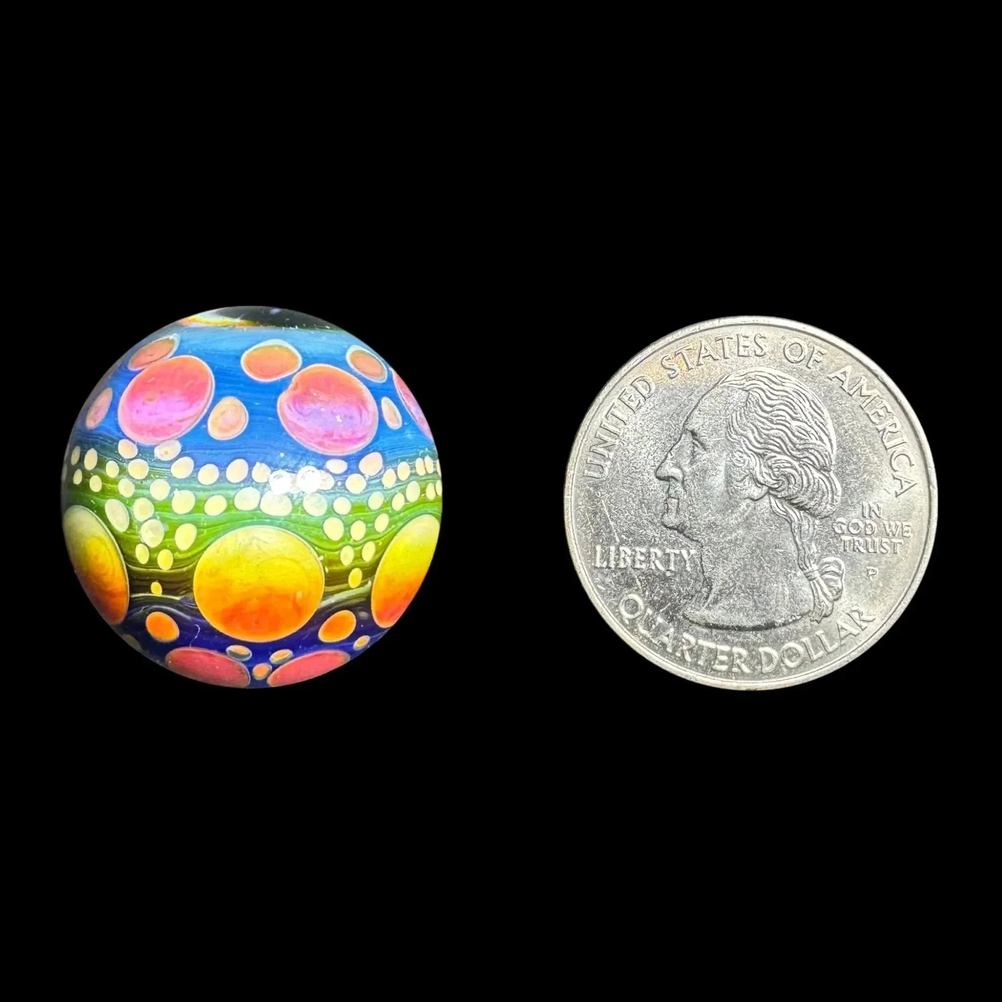 Colorful glass marble with psychedelic dot pattern next to US quarter for size reference