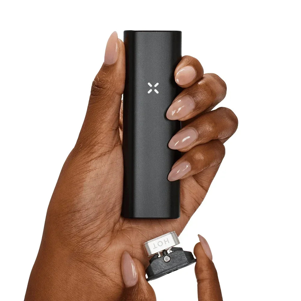 Hand holding a black portable vaporizer with removable cap on white background