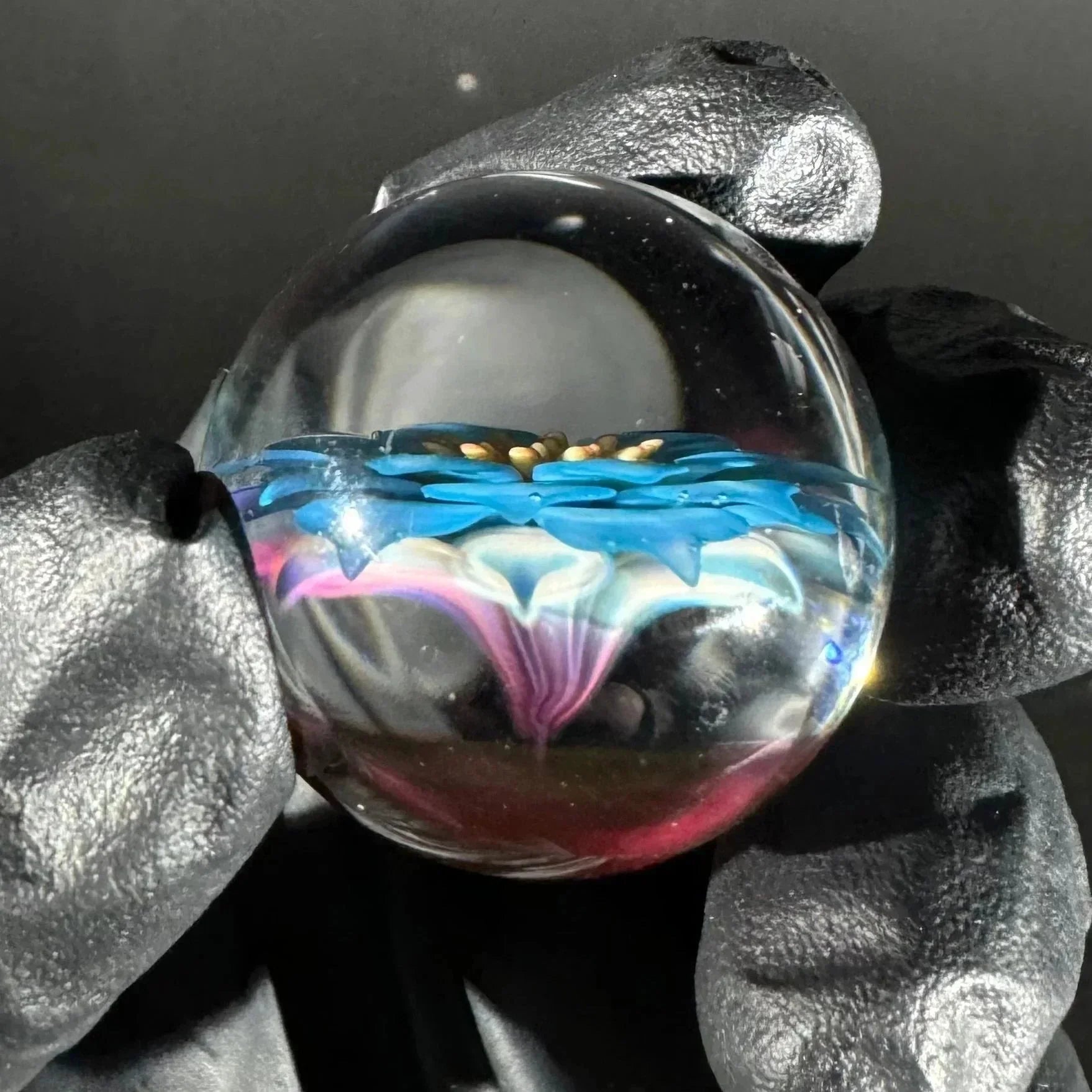 Hand holding a glass marble with intricate blue and pink flower design inside