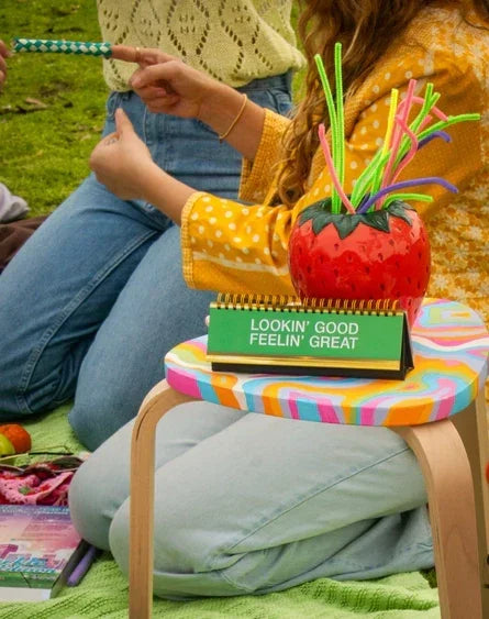 Colorful strawberry-shaped glass accessory with straws on small table at outdoor picnic