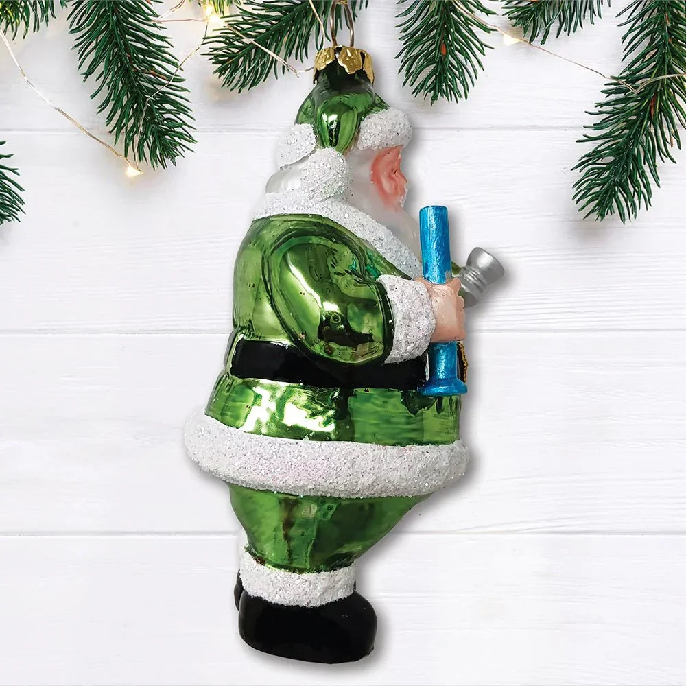 Green Santa figurine holding a blue glass pipe with pine branches on white wood background