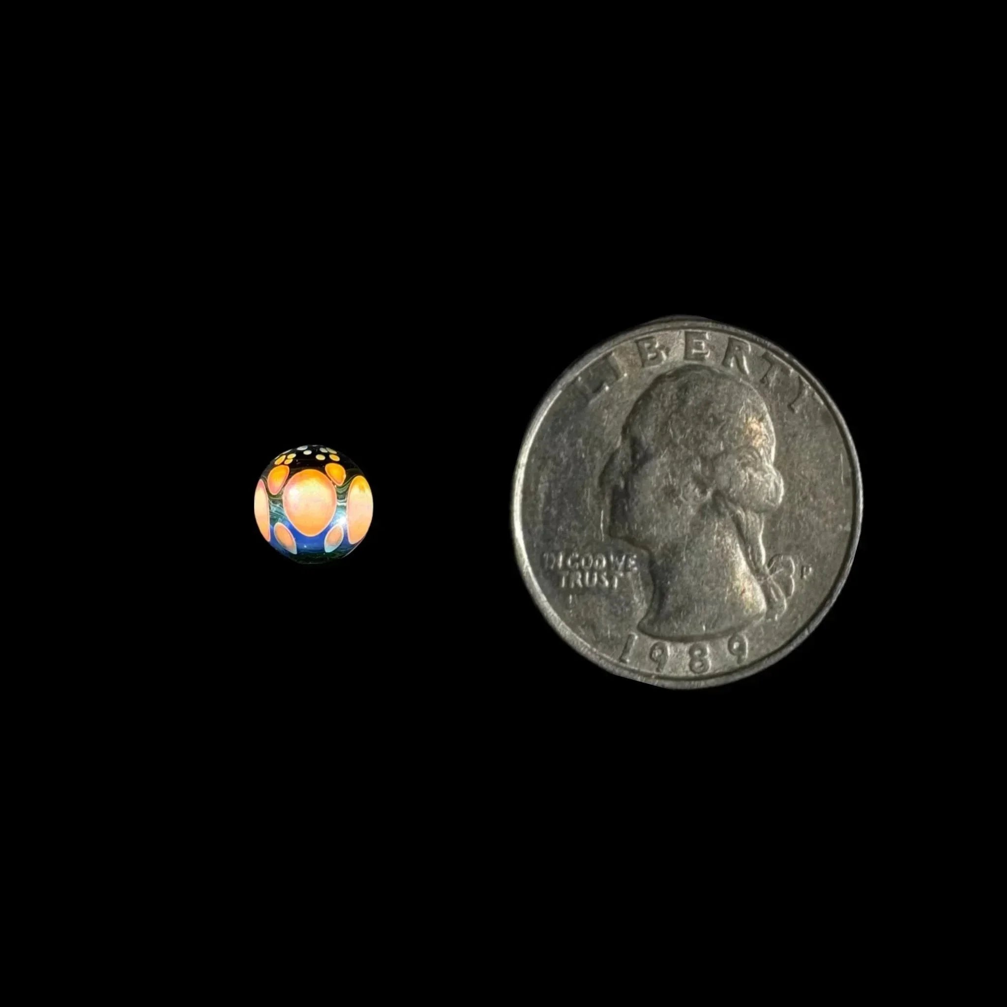 Colorful glass marble with opal detail beside US quarter for size comparison, black background