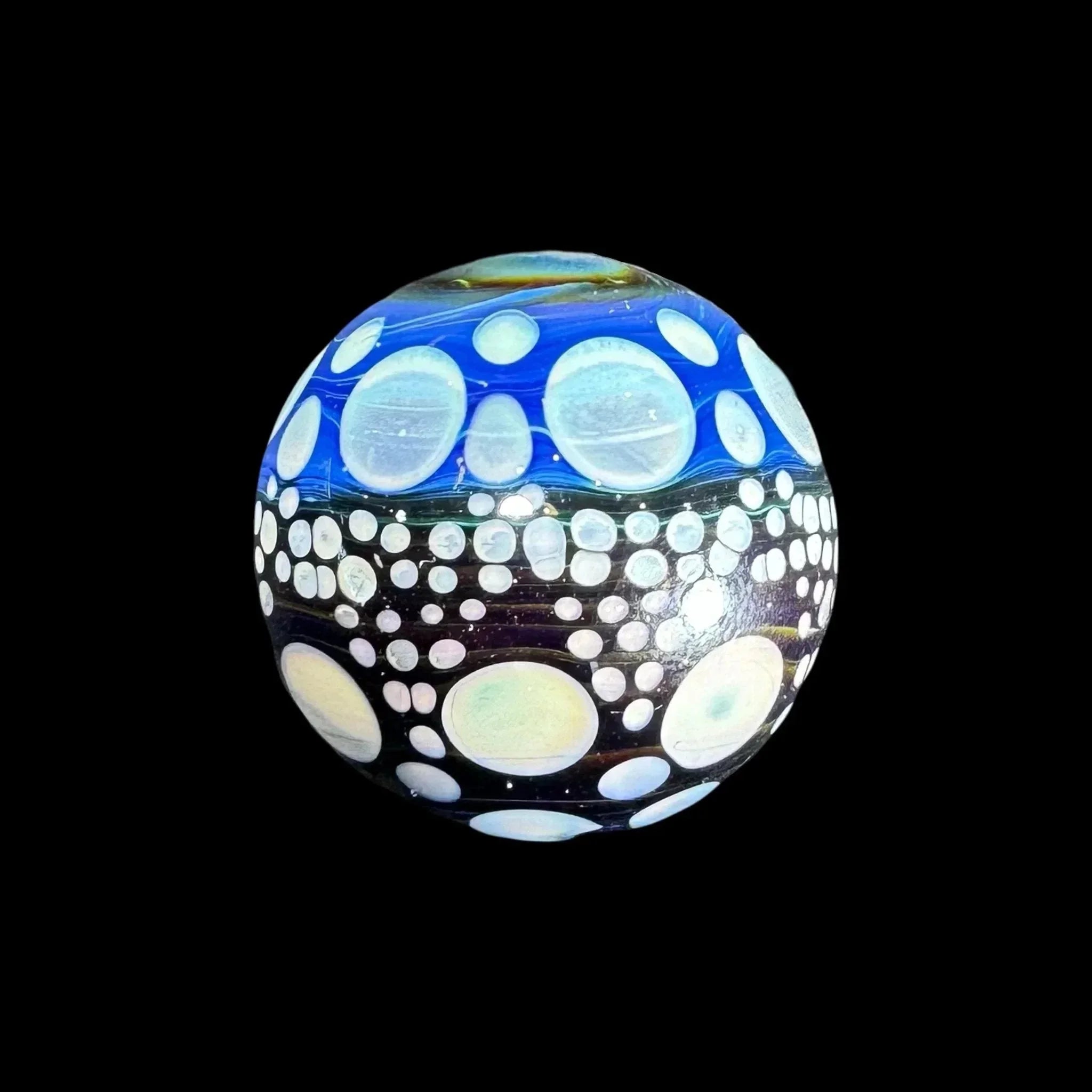 Handcrafted glass marble with blue, black, and white bubble pattern on black background