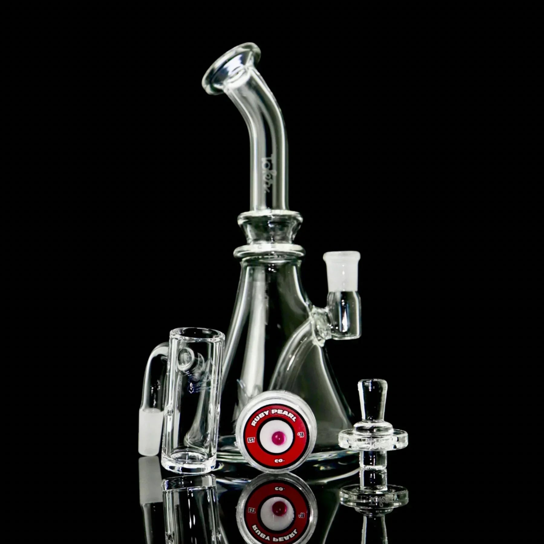 Clear glass dab rig set with accessories, shown on a black background, includes carb cap and banger.