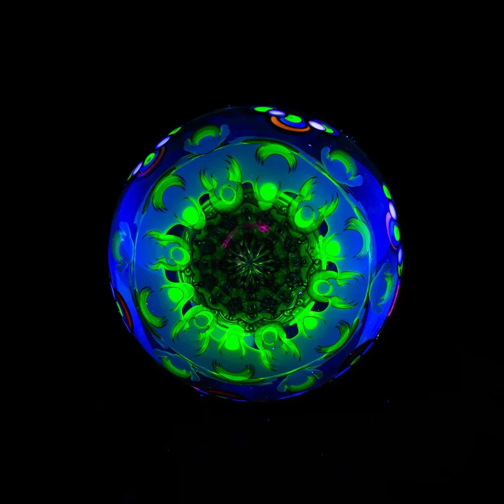UV-reactive glass art sphere with green and blue intricate patterns, glowing on black background