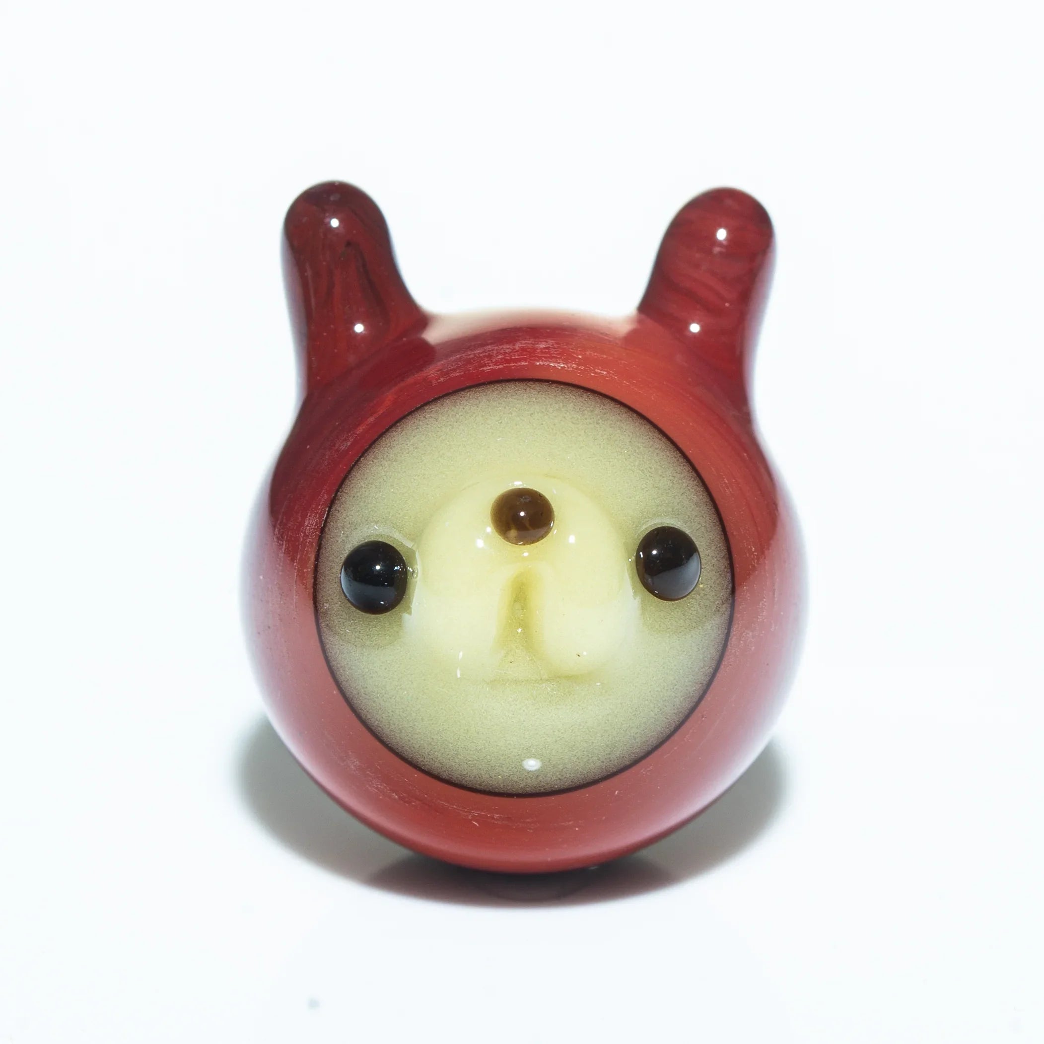 Handblown glass marble in persimmon color with animal face and horns on white background