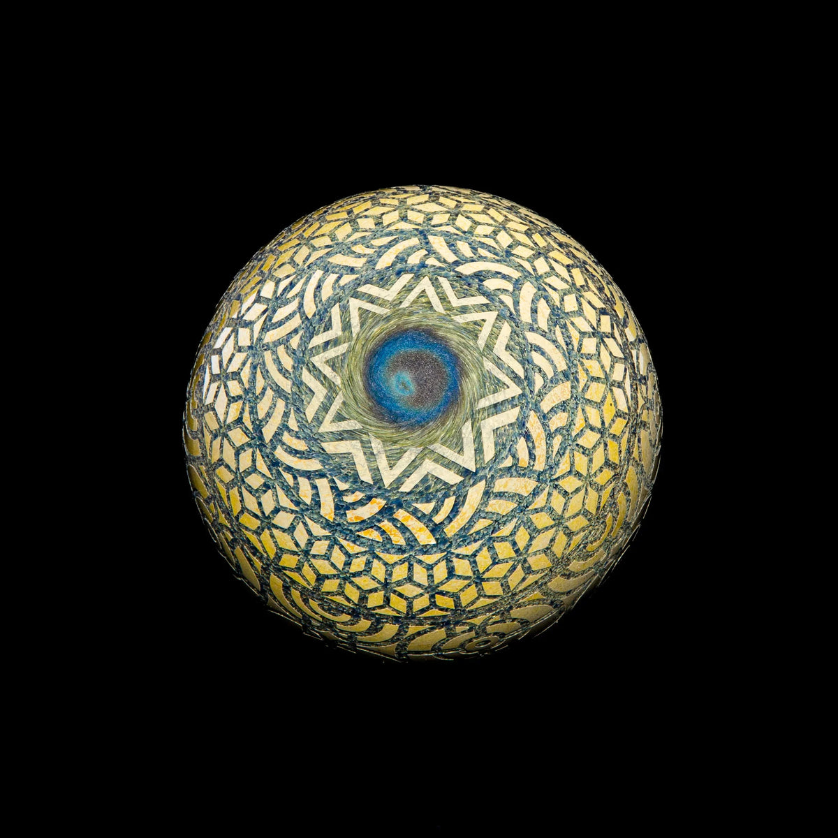 Geometric glass marble with intricate mosaic pattern and blue spiral center on black background.