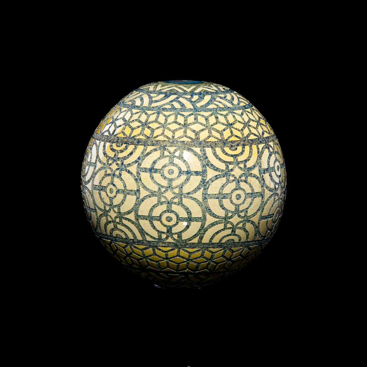 Geometric glass marble with intricate yellow and dark blue circular patterns on black background