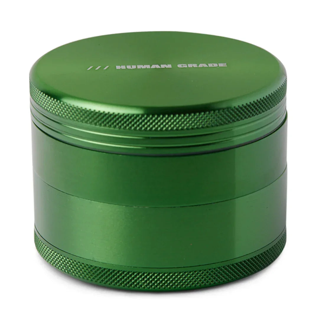 Green metal herb grinder with 'Human Grade' text on lid, textured edges, tabletop display
