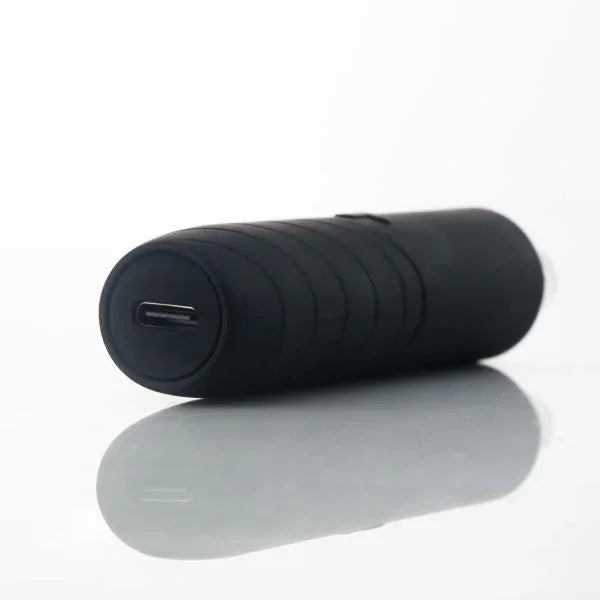 Black portable vaporizer with USB-C charging port on a reflective surface