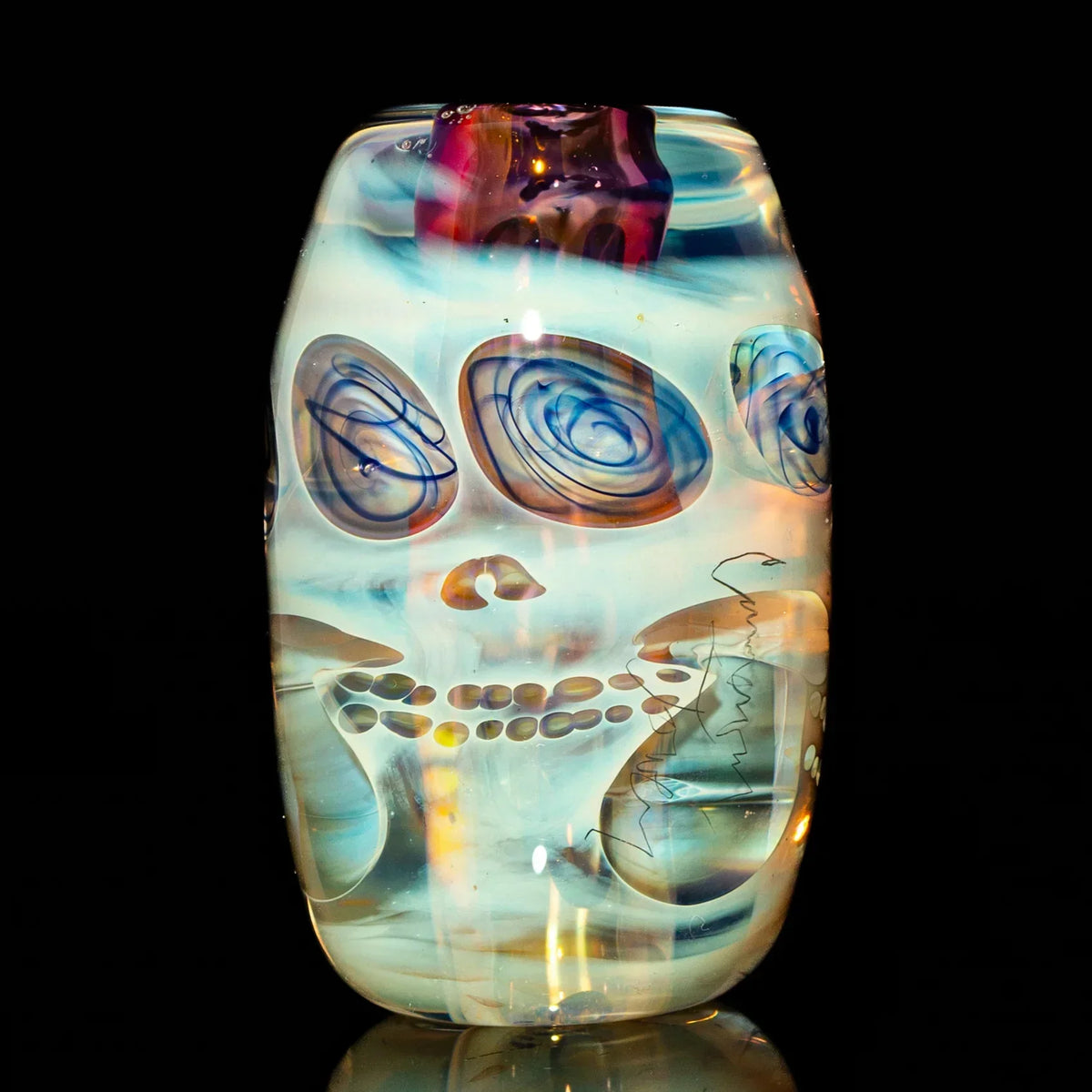 Handcrafted glass art bead with abstract skull design and swirling colors on black background