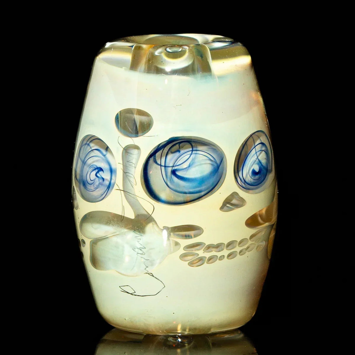 Handcrafted glass bead with blue swirls and skull design on a black background