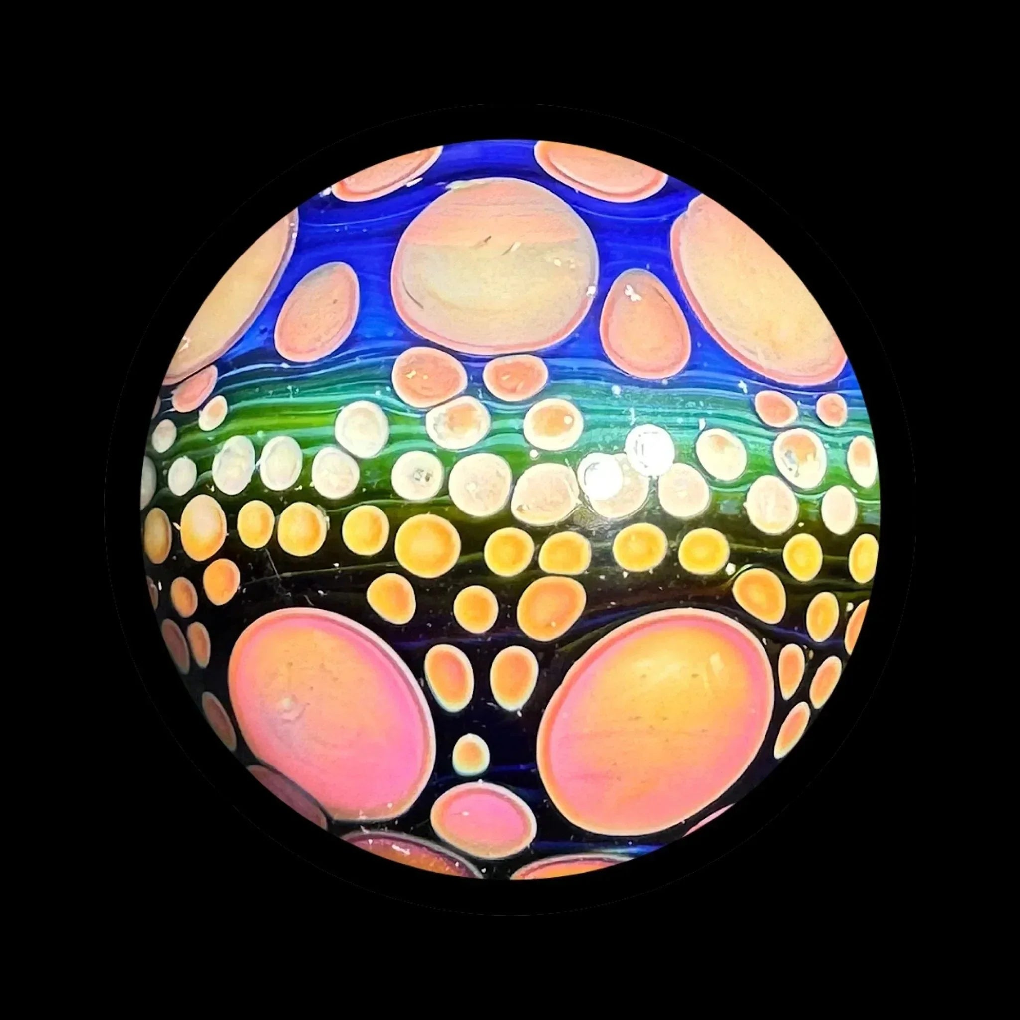 Colorful glass marble with pink and orange bubble patterns on blue and green background