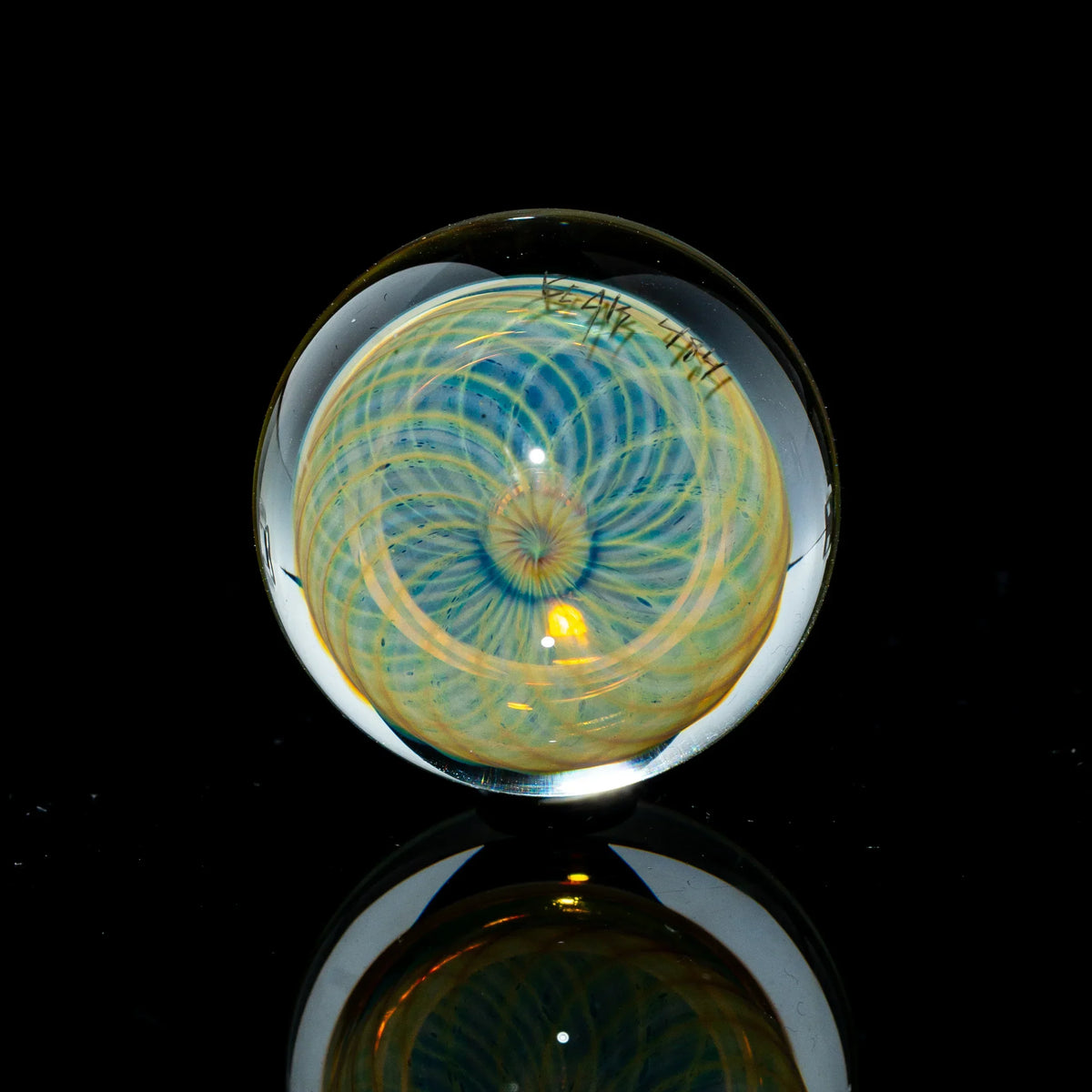 Toroidal glass marble with intricate blue and gold linework design on black background