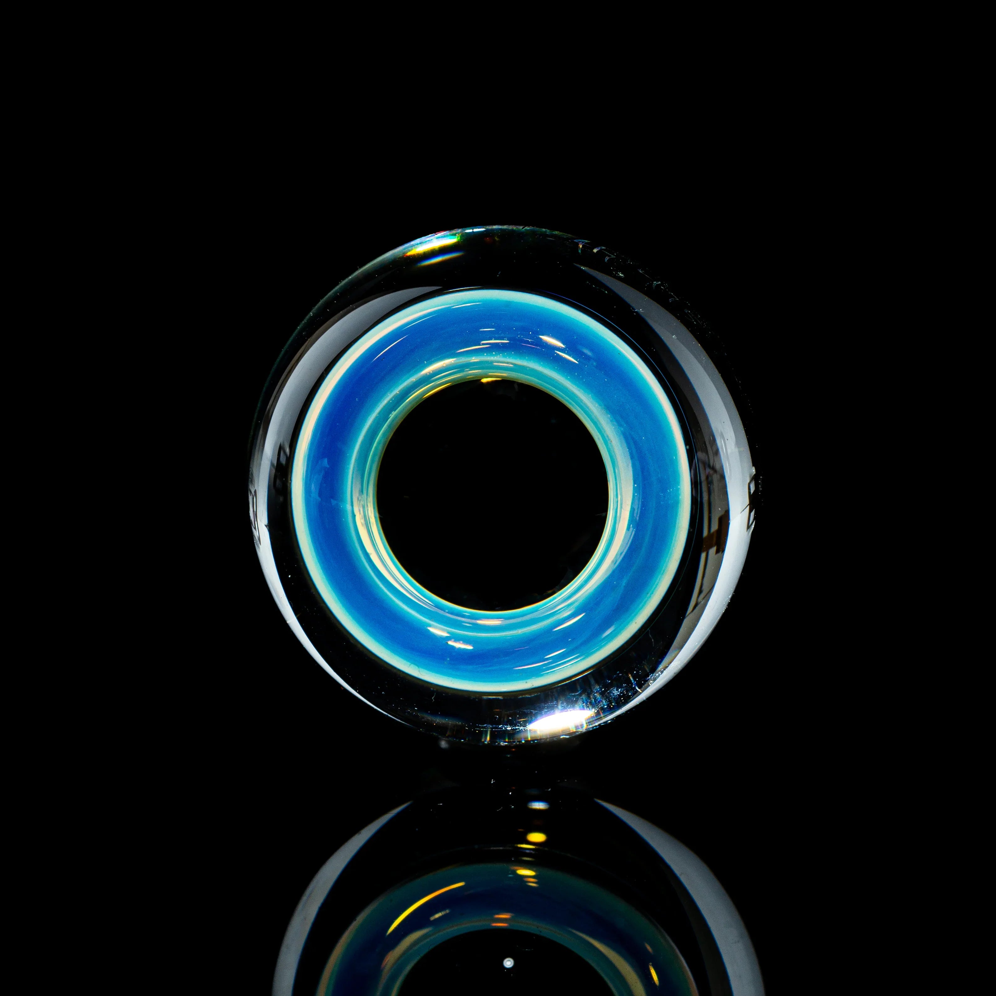 Toroidal top glass marble with blue and yellow rings on black reflective surface