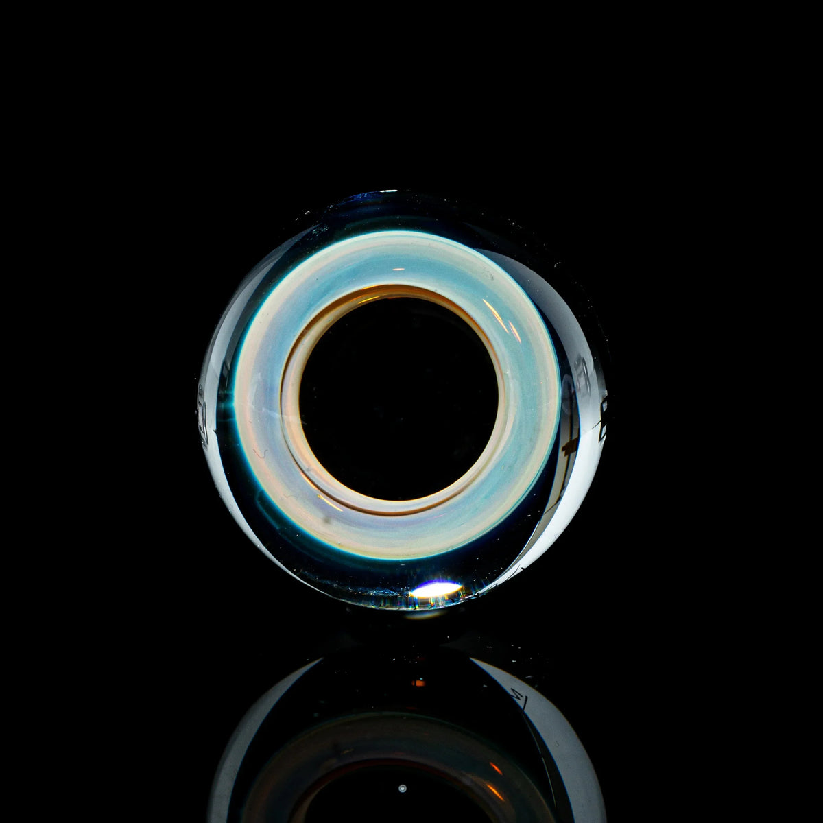 Toroidal glass marble with blue and gold hues on a glossy black background