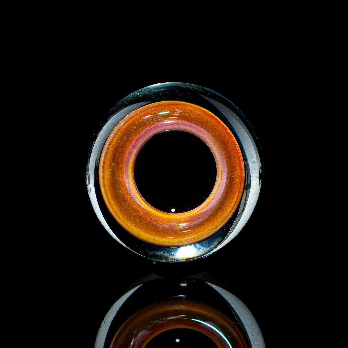 Toroidal glass marble with orange and pink hues on a reflective black background