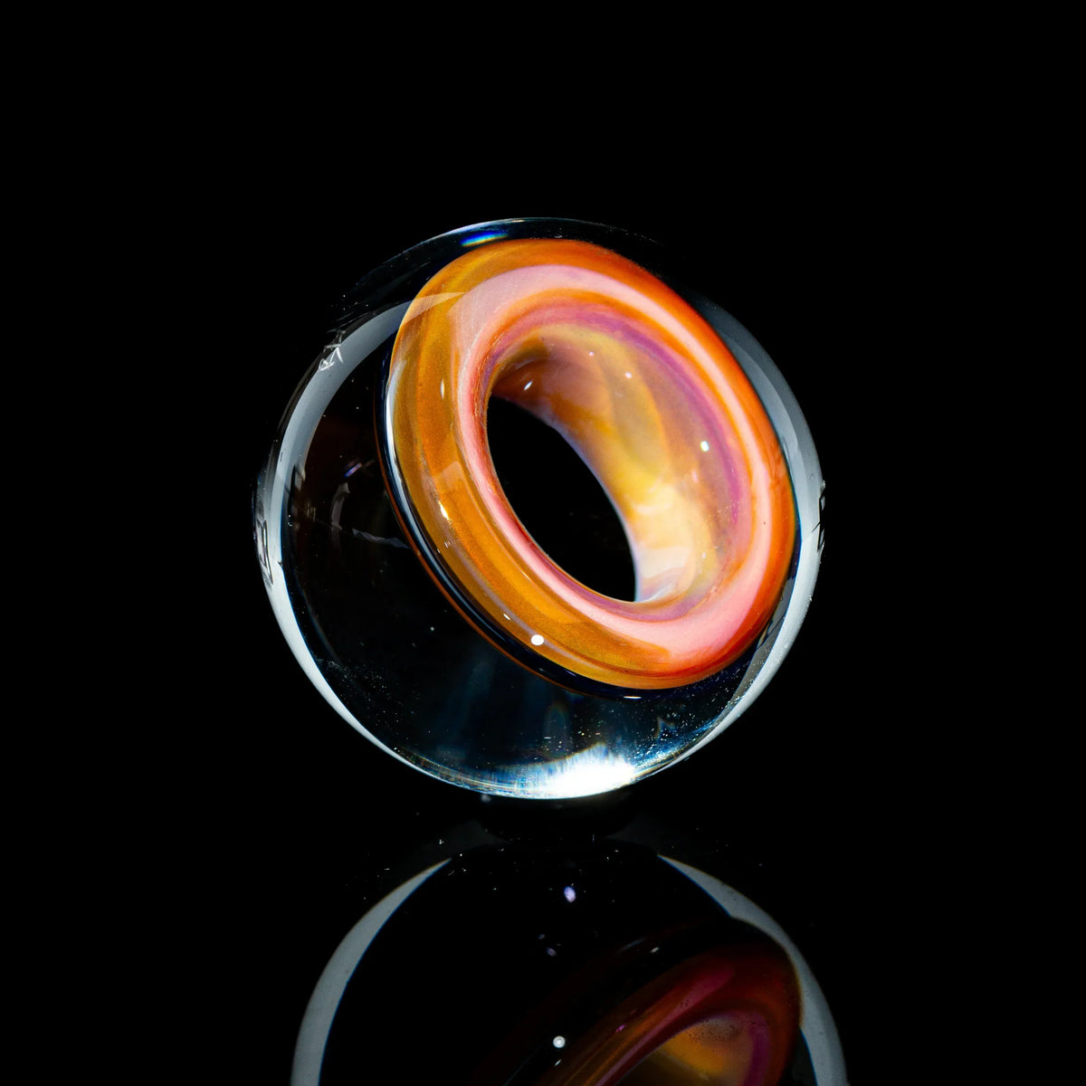Toroidal glass marble with colorful orange and yellow swirls on a black background