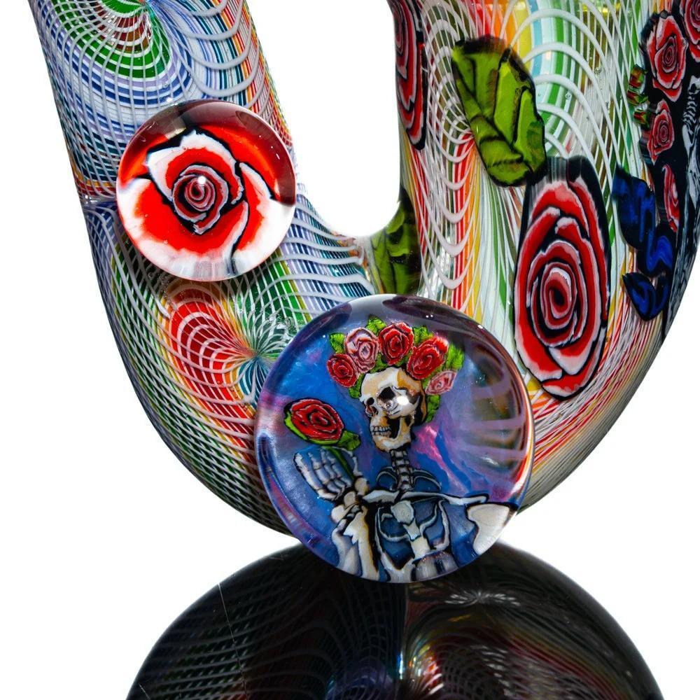 Colorful glass pipe with red rose designs and a skeleton holding roses, rainbow patterns