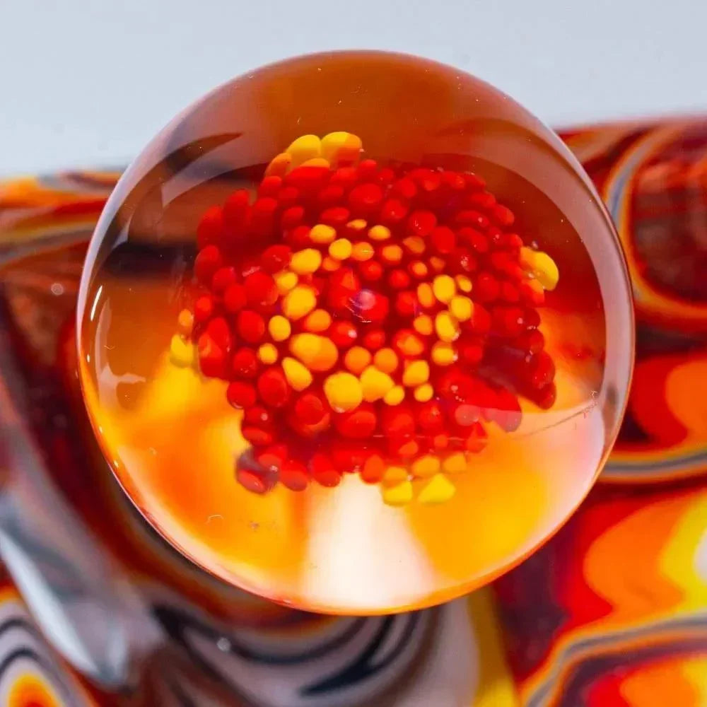 Close-up of an orange and white glass marble with red and yellow implosion design