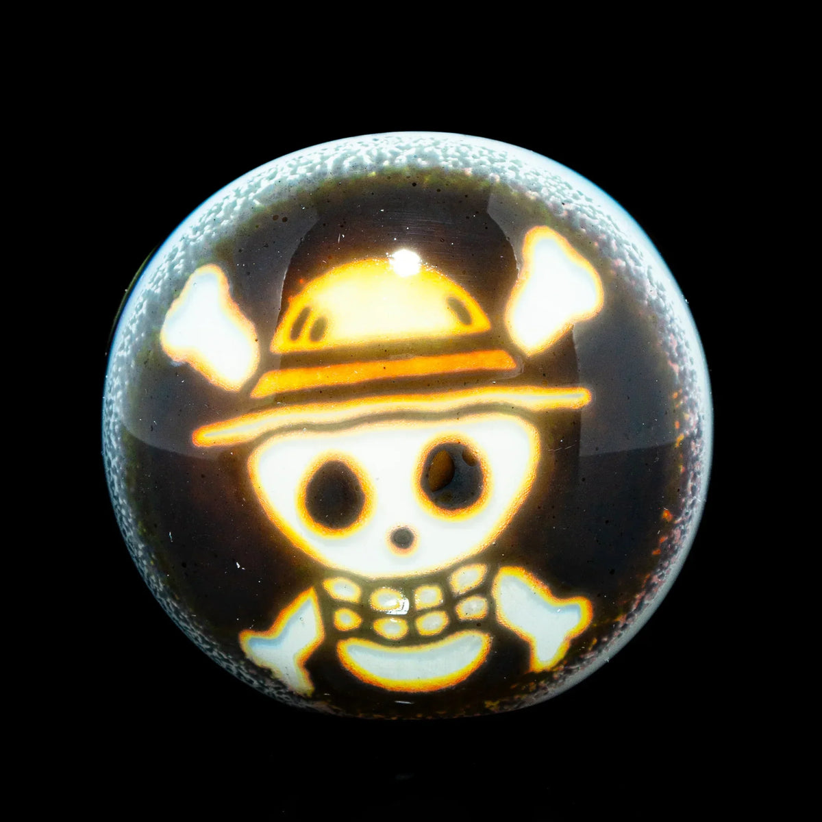 Glass marble featuring a glowing cartoon skull and crossbones with a straw hat design.