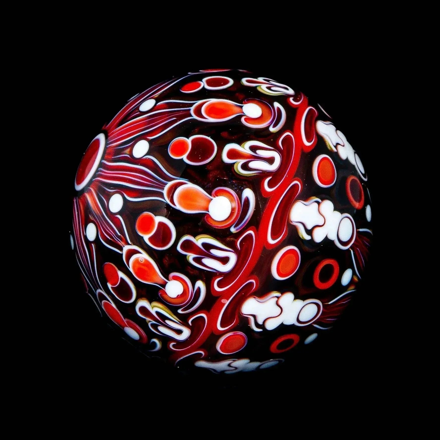 Handcrafted glass marble with intricate red, white, and orange patterns on black background
