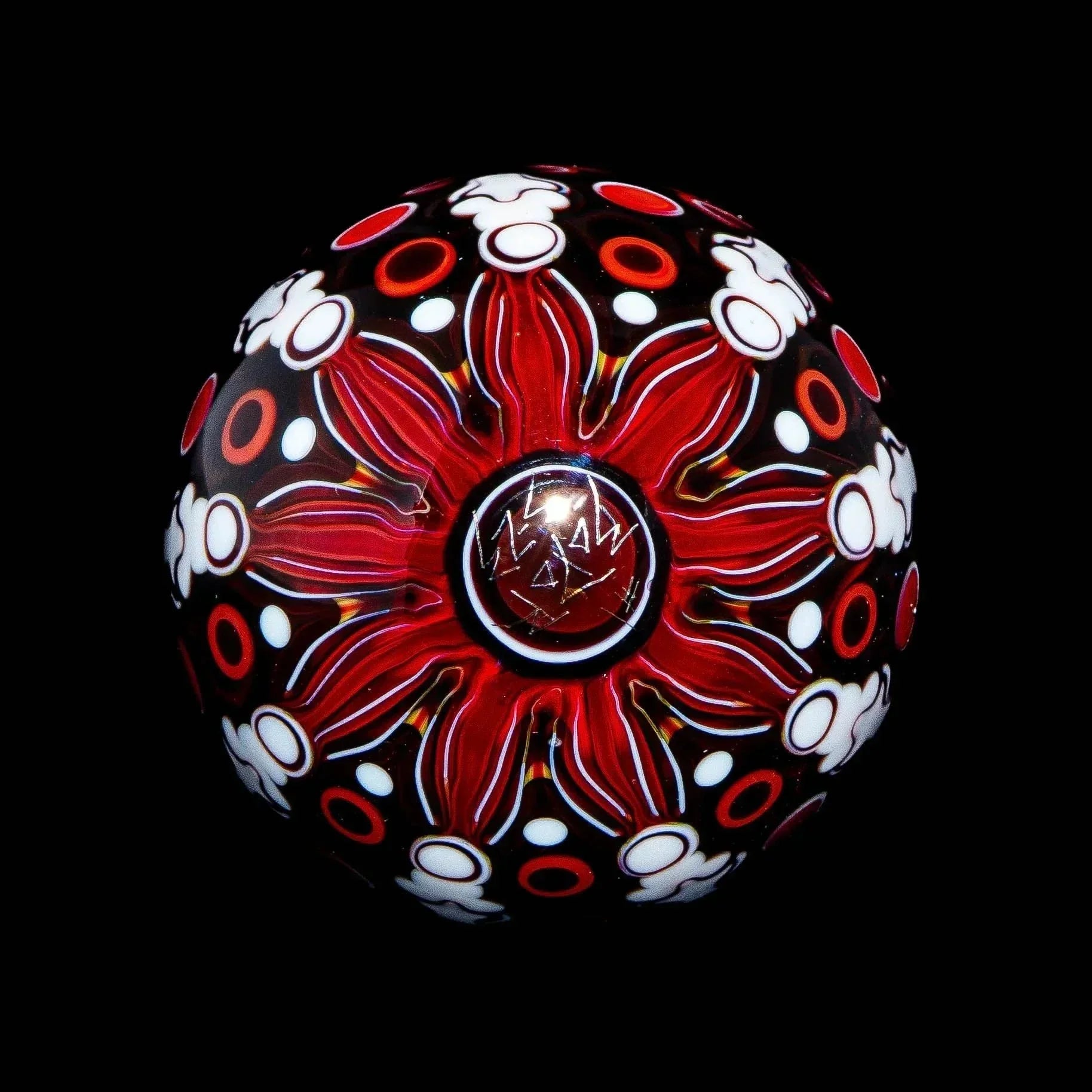 Handcrafted glass marble with intricate red, white, and black flower pattern on black background