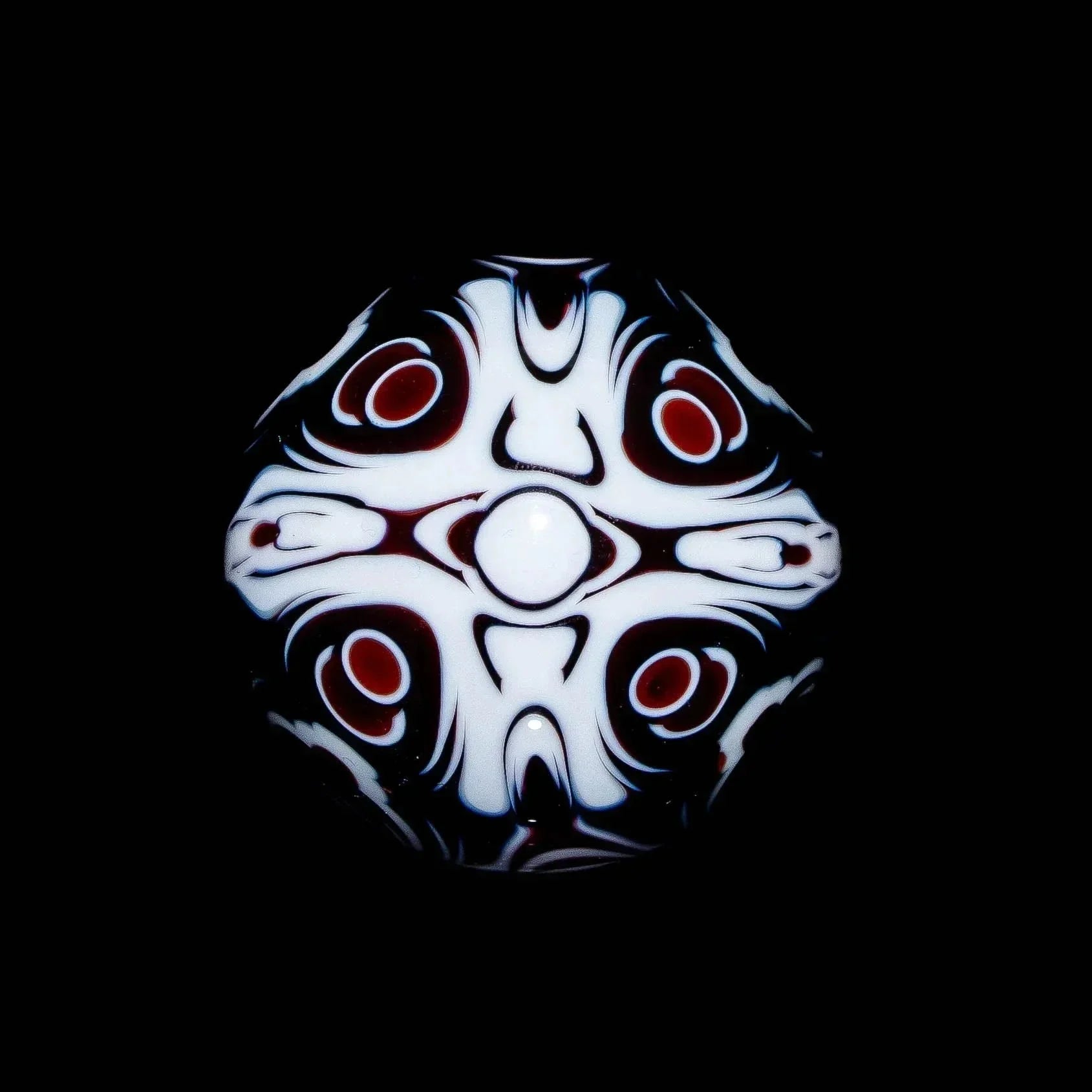 Heady glass marble with intricate black, white, and red abstract patterns on a black background.