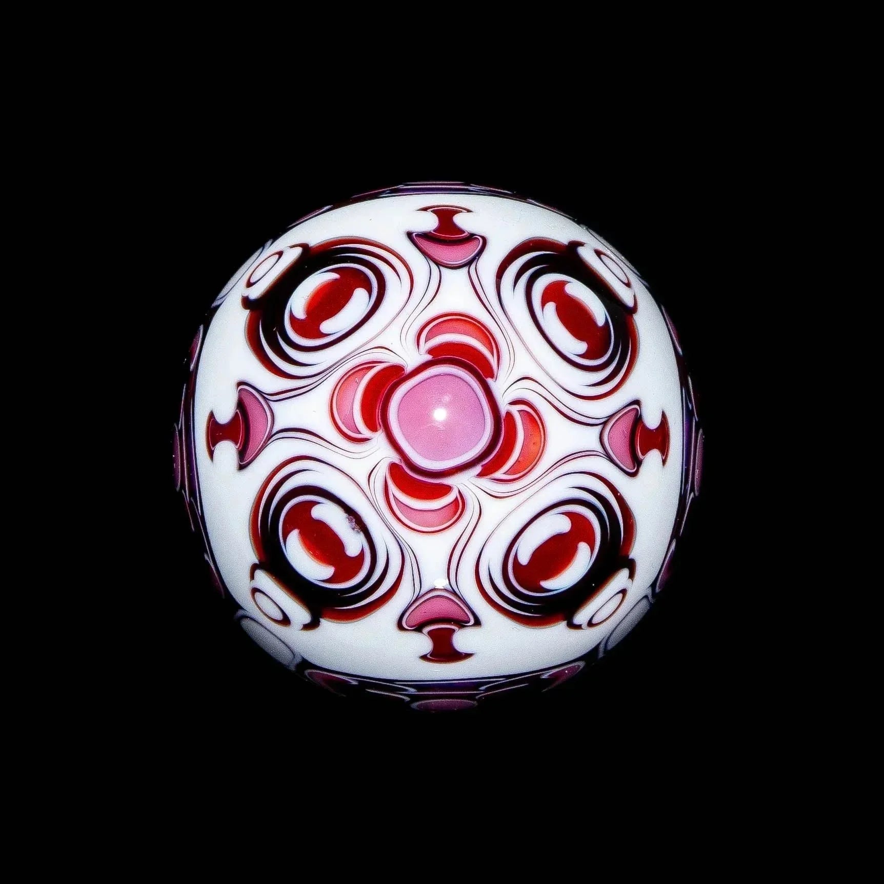 Pink and white glass marble with intricate red swirl patterns on black background