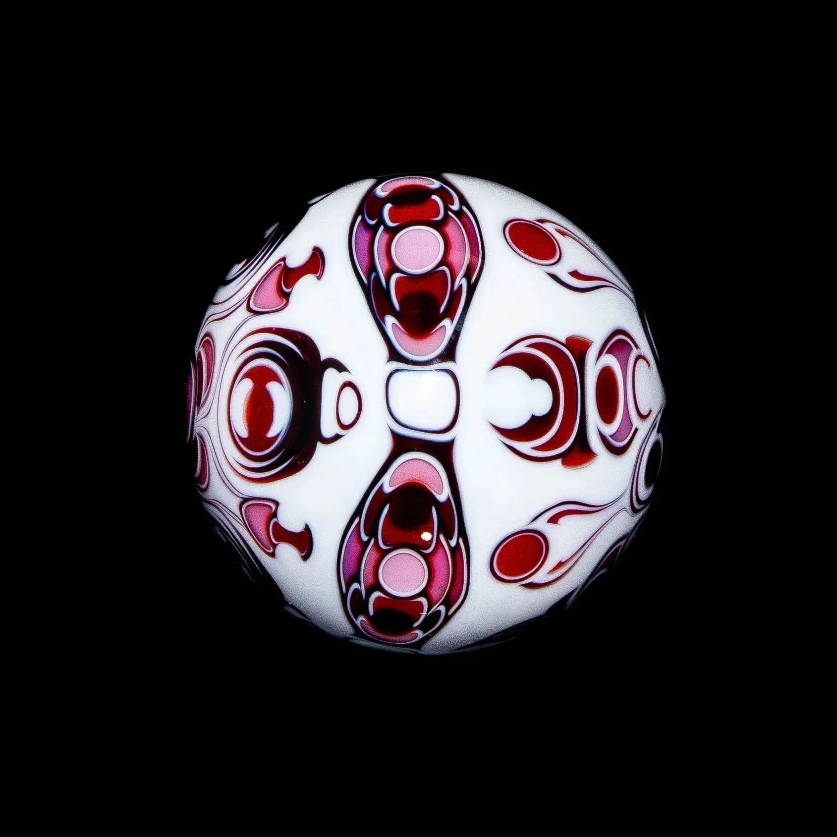 Intricate pink and white glass marble with symmetrical patterns on black background.