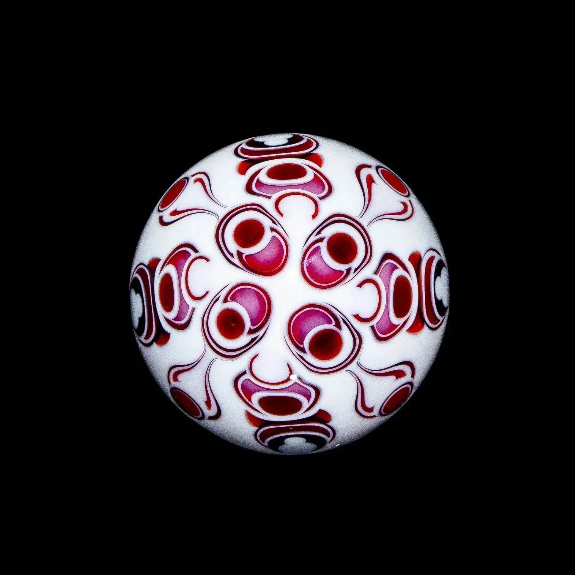 Pink and white glass marble with intricate red and white swirl designs on black background