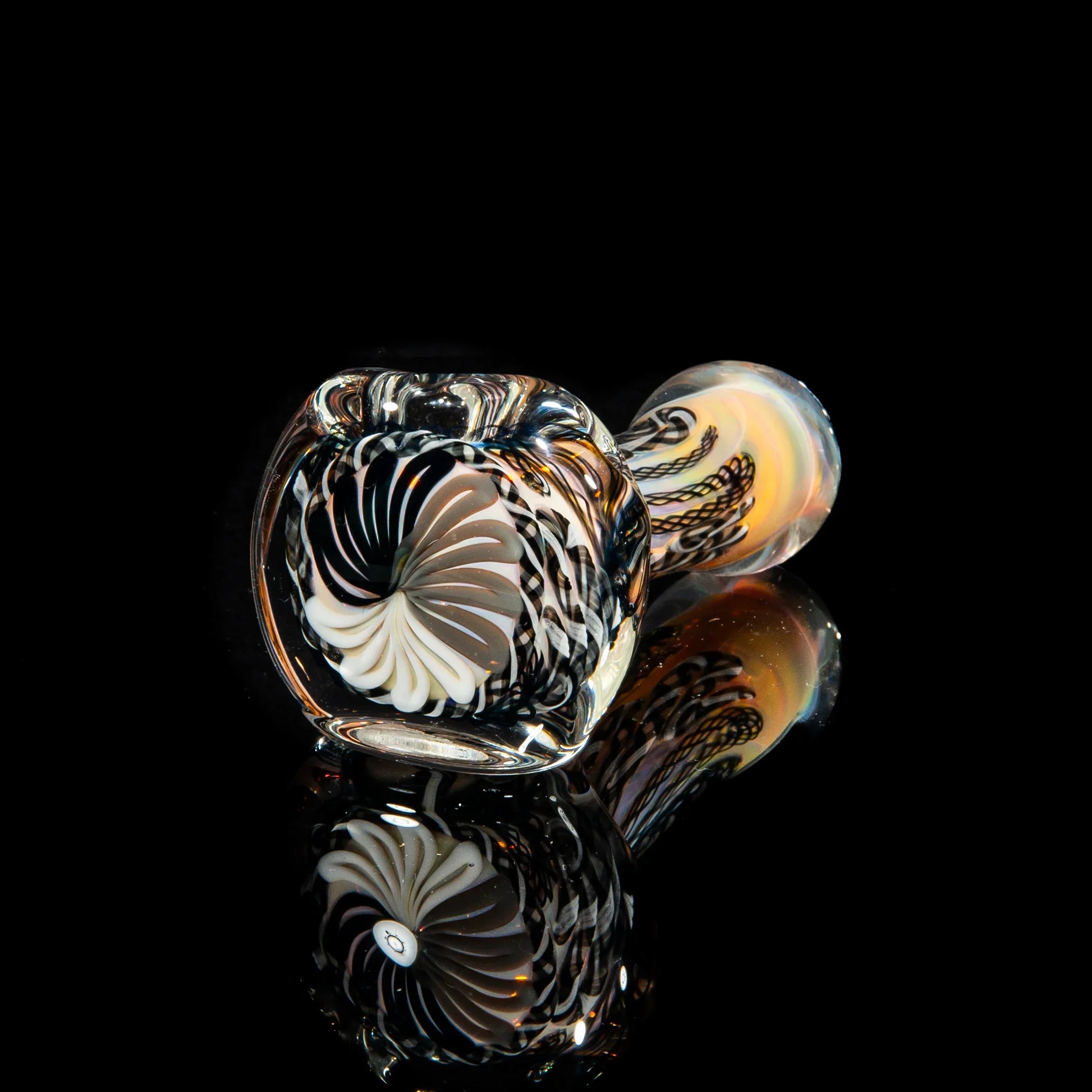 Black and white glass hand pipe with intricate swirl and cane patterns, reflected on black surface.