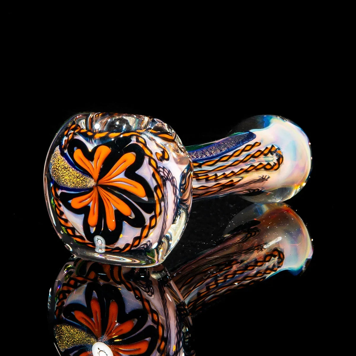 Hand blown glass pipe with orange, gold, and black dichroic accents on a reflective black surface
