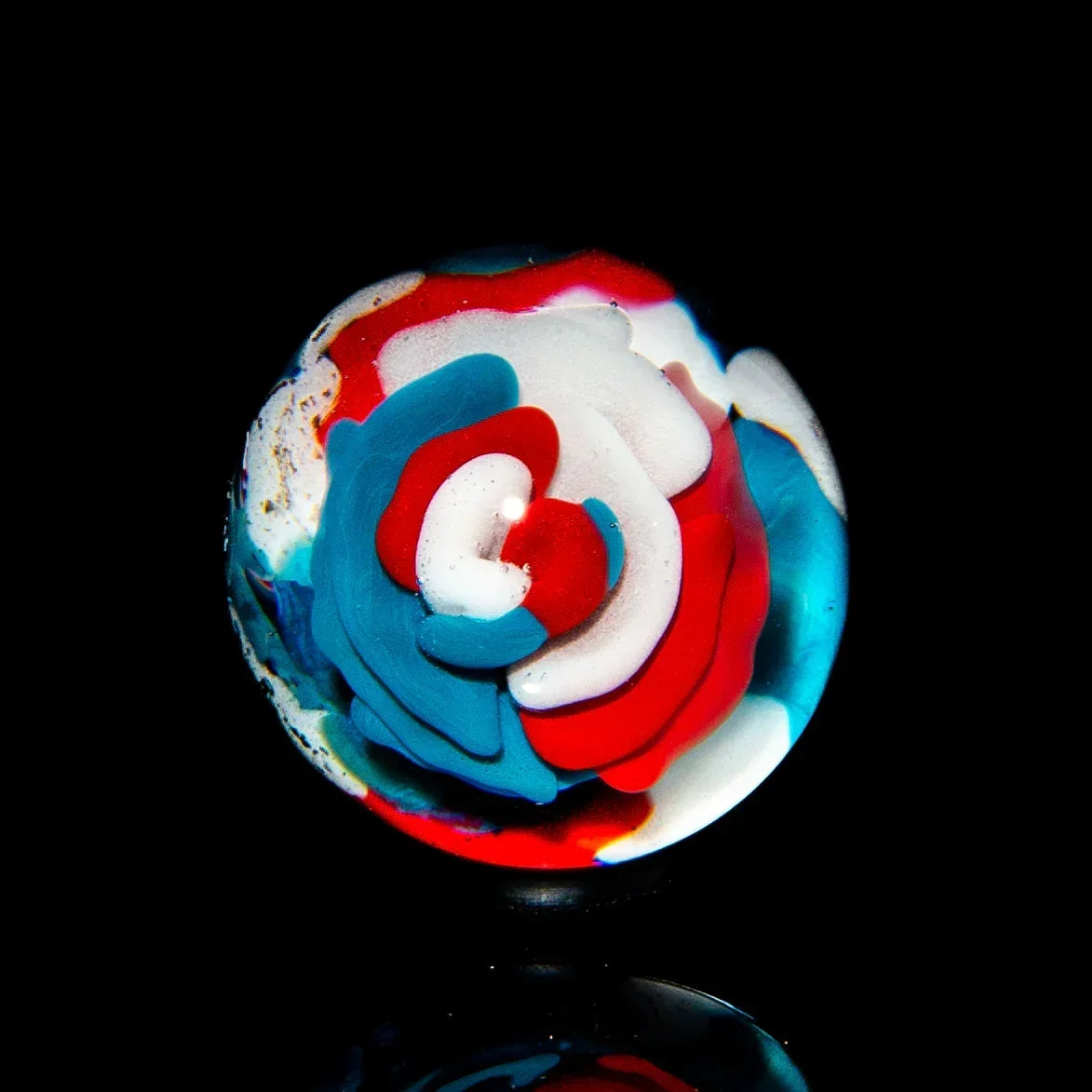 Colorful glass marble with red, white, and blue floral swirl design on black background