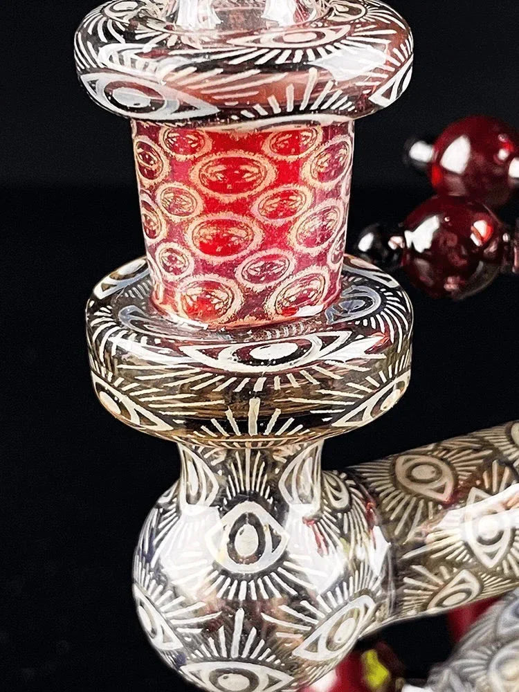 Close-up of a decorative glass pipe with intricate eye patterns and red accents